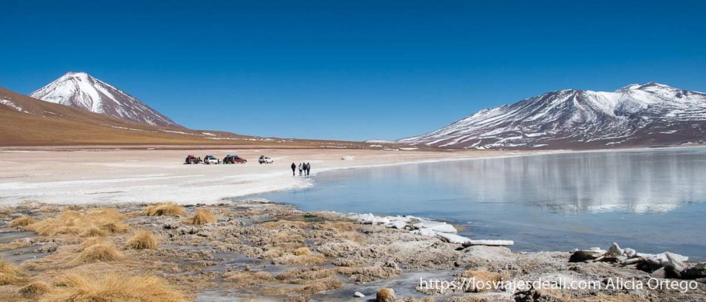 Evitar el mal de altura: consejos desde la experiencia 8 laguna blanca de bolivia con agua azul claro que refleja volcán nevado, orilla blanca con personas andando y coches 4x4 parados al lado consejos para evitar el mal de altura