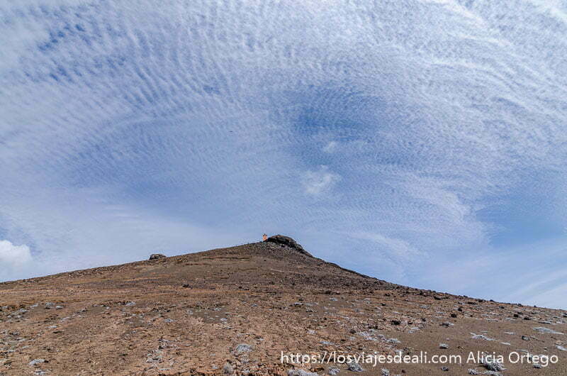 cumbre de isla bartolomé con un faro naranja y muchas nubes en el cielo