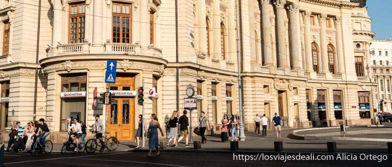 gente andando junto a edificio neoclásico iluminado por luz cálida en bucarest