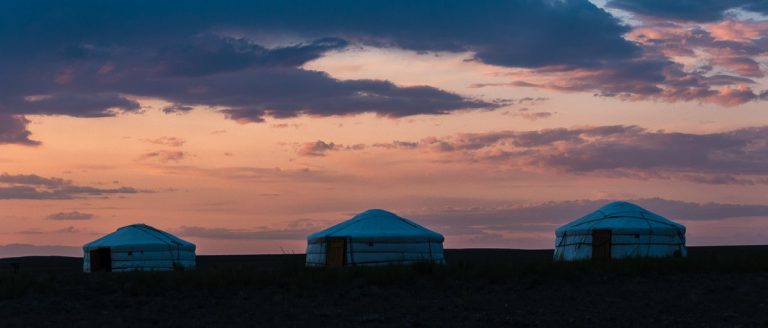 Primeras impresiones de un viaje a Mongolia 9 tres gers se recortan en el horizonte con colores y nubes de atardecer en el viaje a mongolia