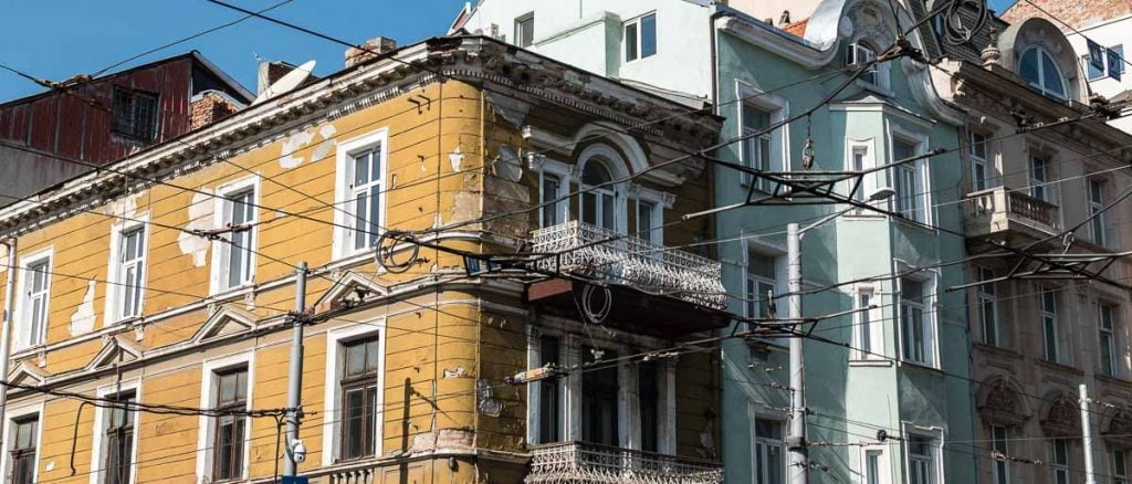 esquina de edificios antiguos pintados de color amarillo y verde desconchados con cables de tranvía en sofía