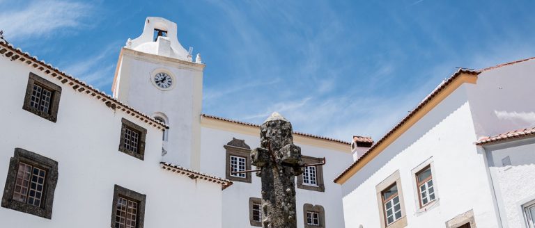 picota de piedra rodeada de casas blancas con ventanas de piedra y torre de iglesia con reloj en marvao portugal