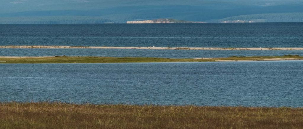 lago khovsgol desde la orilla con isla al fondo y montañas con bosques al otro lado