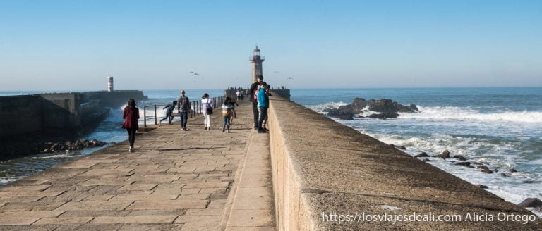 faro al fondo del espigón con el mar y personas paseando