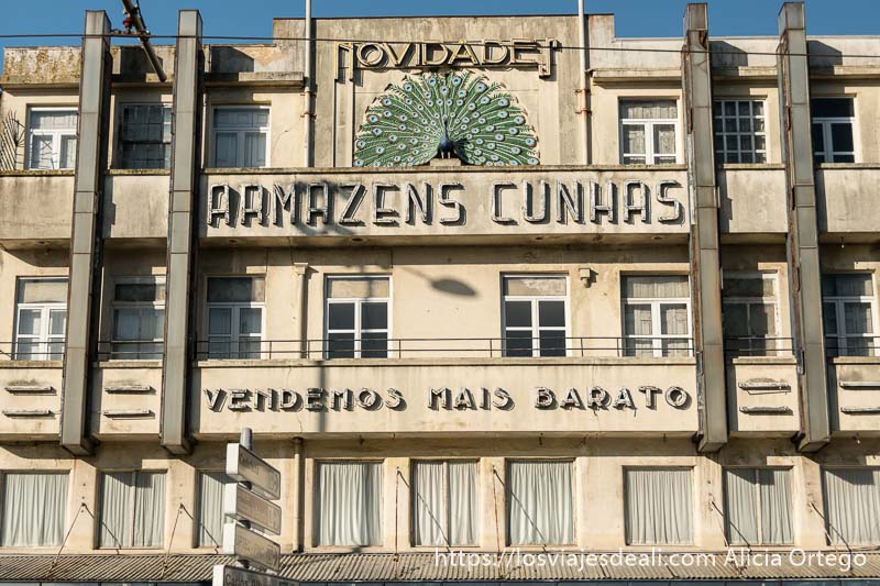 fachada de edificio modernista con cartel de unos almacenes de los años 70 y un pavo real como símbolo en oporto