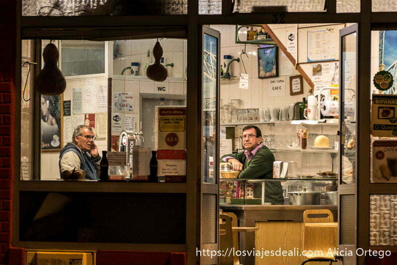 dos hombres dentro de un bar por la noche, uno hablando por el móvil y el otro mirando la tele en oporto