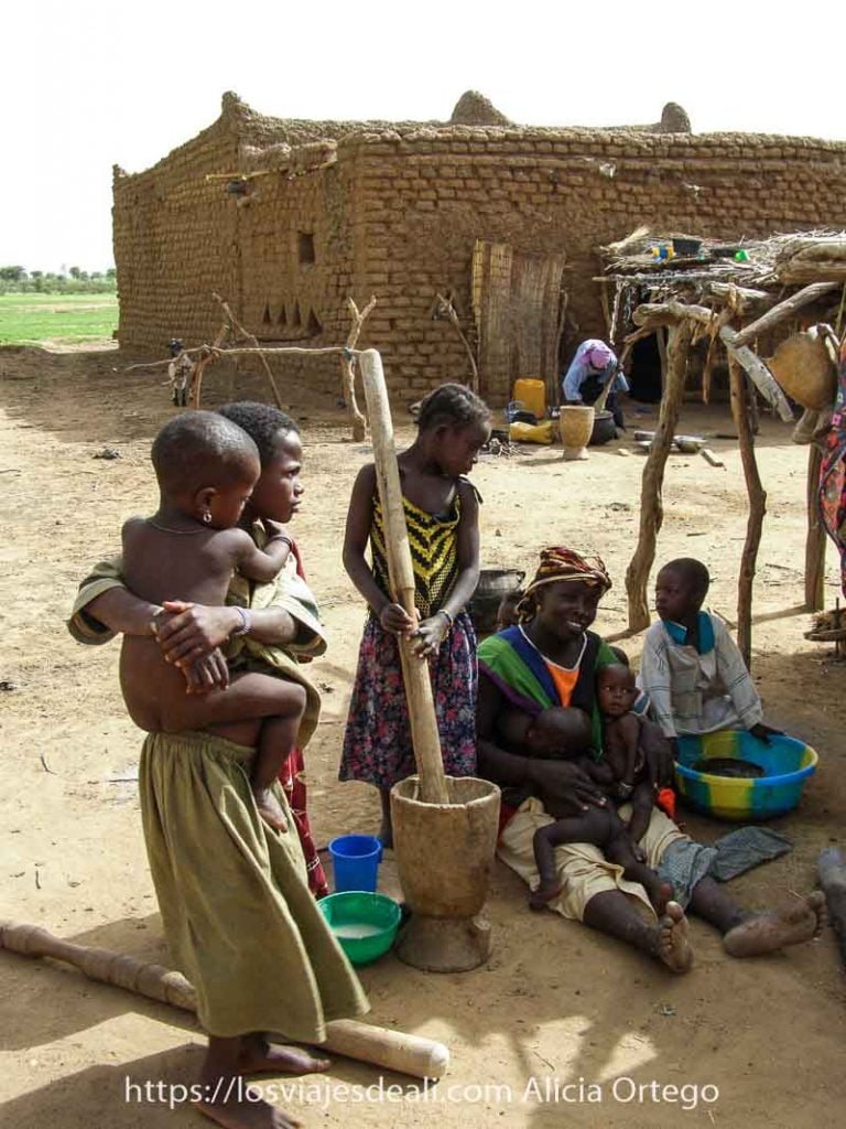 Mi primer mercado africano en el Sahel de Burkina Faso: Gorom Gorom 56 mujeres sentada en el suelo con dos bebés mellizos amamantándolos y una niña moliendo mijo a su lado con un gran palo