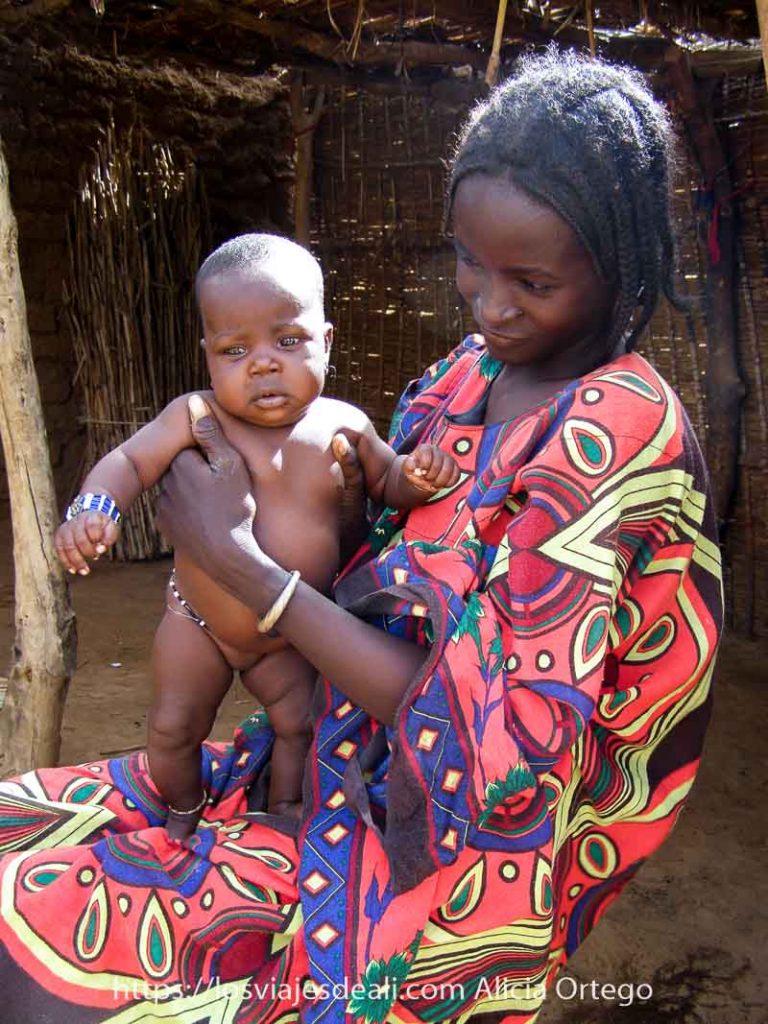 Mi primer mercado africano en el Sahel de Burkina Faso: Gorom Gorom 57 chica joven con pelo de trenzas y su bebé gordito y desnudo sobre el regazo del vestido de colores