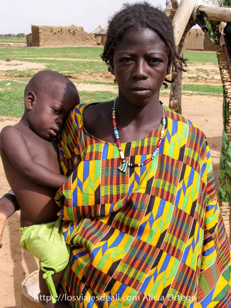 Mi primer mercado africano en el Sahel de Burkina Faso: Gorom Gorom 58 chica joven bella con vestido de colorines y collar de piedras de colores y su bebé apoyado en la cadera