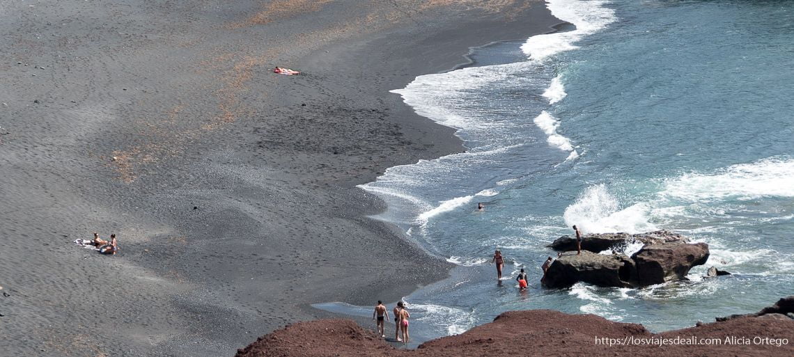 plaza de arena negra con gente bañándose en la costa oeste de lanzarote
